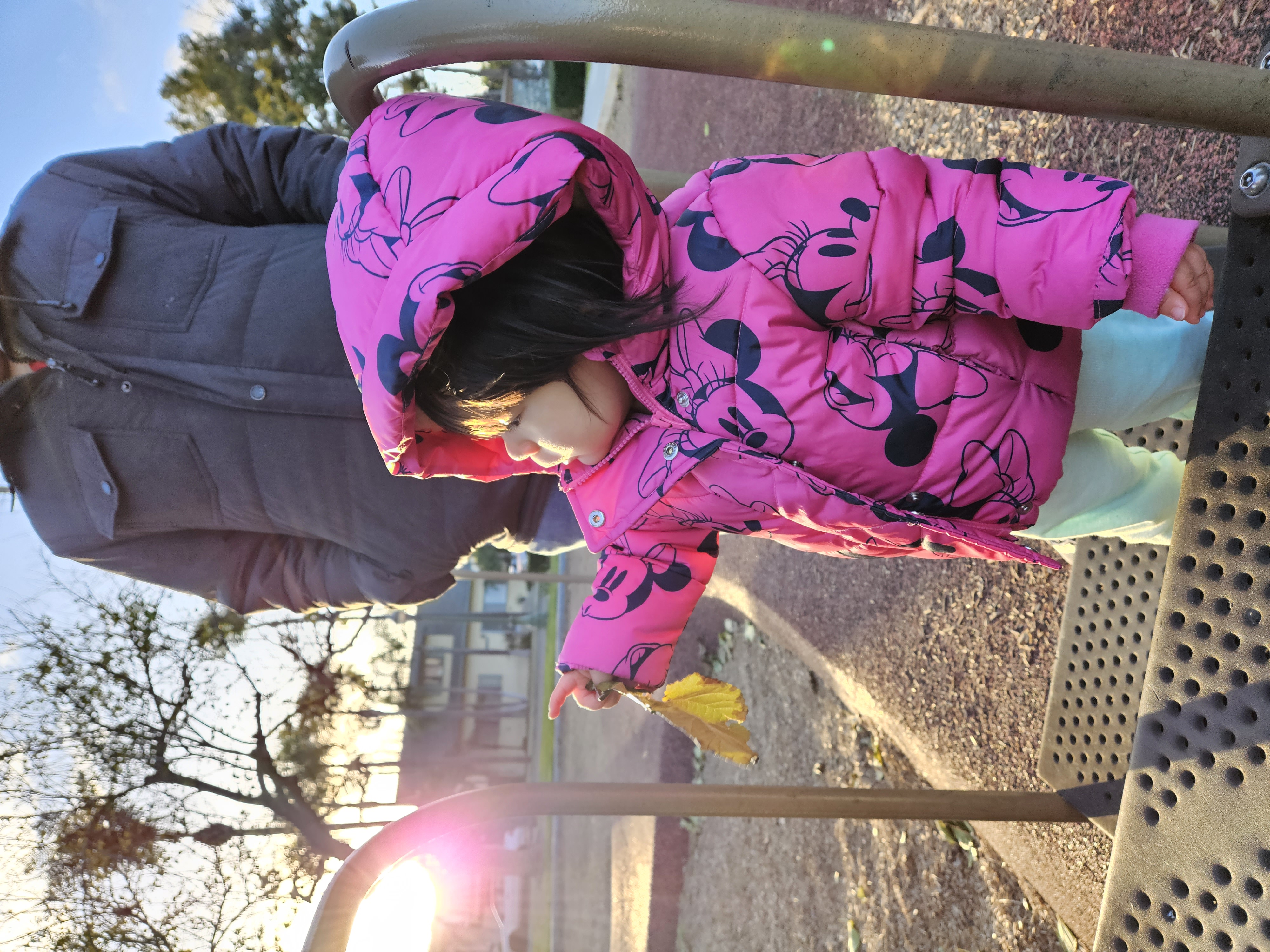 Toddler in pink puffy Minnie Mouse jacket holding a leaf taken with Samsung Galaxy S23